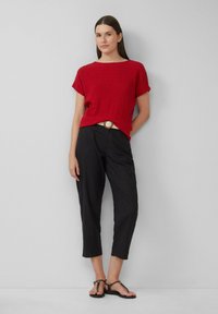Haut à manches courtes texturé rouge associé à un pantalon cropped noir et des sandales noires. Une ceinture de teinte claire accentue la taille.