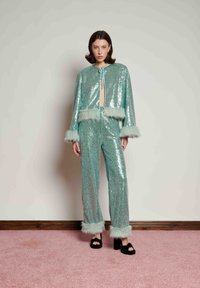 Shiny mint green sequin set with a cropped jacket featuring fur trim and matching pants. High-heeled black sandals complete the outfit.
