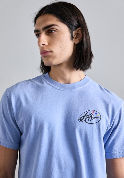 Light blue cotton t-shirt with a round neckline and short sleeves. Features a logo on the left chest with colorful dots. Soft texture.