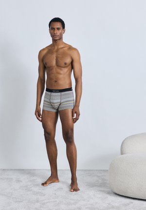 Boxers courts rayés en mélange de coton, avec une ceinture noire. Couleurs comprenant des rayures grises, jaunes et blanches. Modèle debout pieds nus.