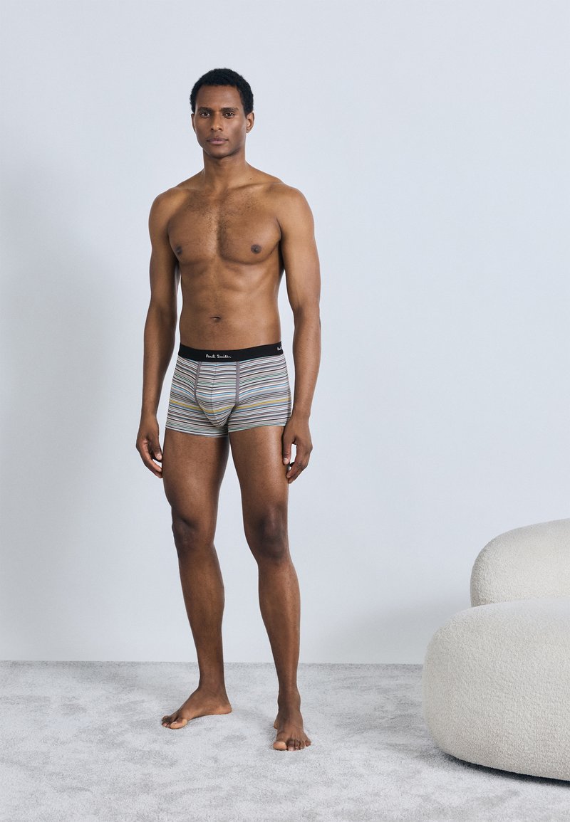 Ριγέ ανδρικά μπόξερ από βαμβακερό μείγμα, με μαύρη μέση. Τα χρώματα περιλαμβάνουν ρίγες σε γκρι, κίτρινο και λευκό. Το μοντέλο στέκεται ξυπόλητο.