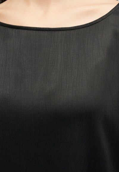 Krupan plan crnog teksturiranog platnenog topa sa širokim, zaobljenim dekolteom i vidljivim šavovima uz rub.