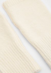 Mănuși din lână tricotate, de culoare crem, cu manșete ribbate și un finisaj moale, texturat, având o formă ușor supradimensionată.