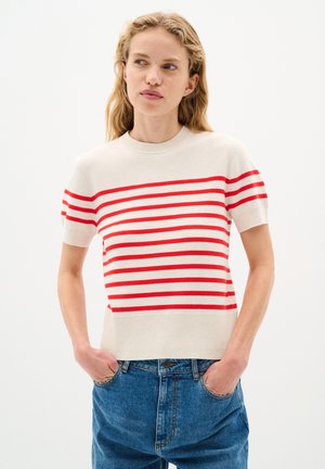 Helles beiges Strickpullover mit roten horizontalen Streifen, kurzen Ärmeln, rundem Hals und fitted Saum. Kombiniert mit blauen weit geschnittenen Jeans.