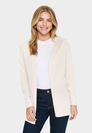 Cardigan beige à manches longues, ouvert à l'avant et à coupe décontractée, associé à un t-shirt blanc et un jean en denim foncé. Texture douce.