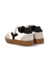 Zapatilla blanca y gris con un acento negro, que cuenta con una correa de Velcro, materiales de ante y cuero liso, y una suela de goma marrón.