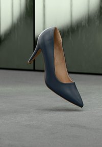 Γόβα από μπλε σκούρο δέρμα λουστρίνι με μυτερή μύτη, λεία επιφάνεια και λεπτό, κομψό τακούνι. Το εσωτερικό διαθέτει ανοιχτό καφέ φόδρα.