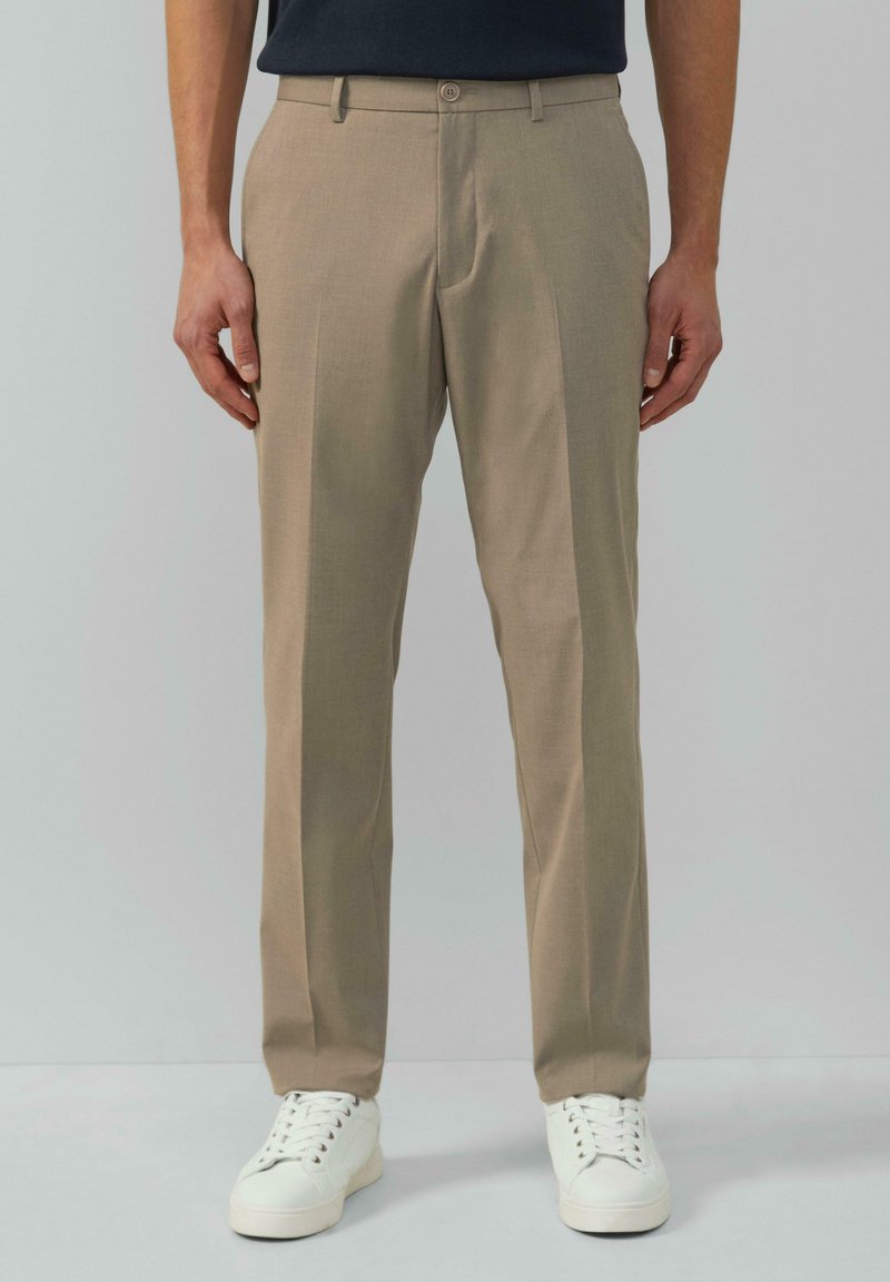 Beige maßgeschneiderte Stoffhosen aus leichtem Material mit Knopfverschluss, seitlichen Taschen und geradem Bein, kombiniert mit weißen Sneakers.