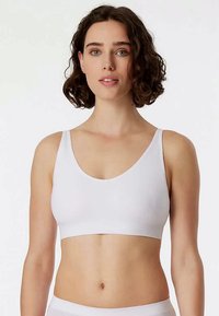 Hvid sømløs bralette med scoop-udskæring og brede stropper, der har en blød, glat tekstur og et tætsiddende, minimalistisk design.