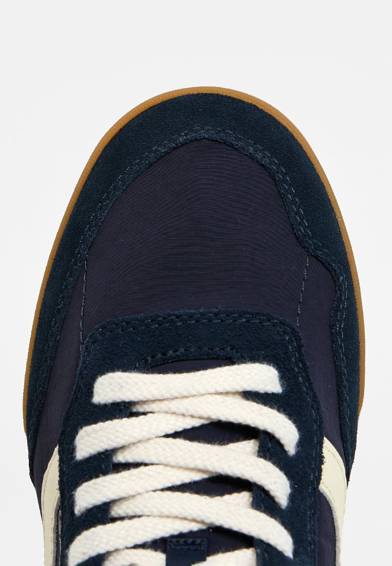 Sneaker blu navy con upper in tessuto texture, dettagli in suede, lacci color crema e suola in gomma marrone. Design atletico classico.