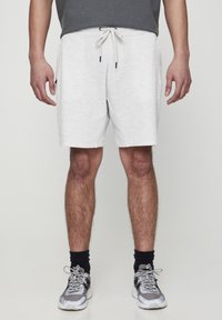 Shorts de sport légers gris clair pour homme, avec une taille élastique, un cordon de serrage et des poches latérales. Portés avec des baskets grises et des chaussettes noires.