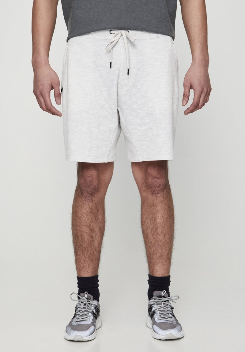 Shorts de sport légers gris clair pour homme, avec une taille élastique, un cordon de serrage et des poches latérales. Portés avec des baskets grises et des chaussettes noires.