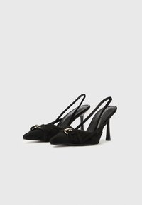 Melni zamšādas smailiem purngaliem ar plānām siksniņām un spīdīgu metāla akcentu uz augšpuses. Augsts stiletto papēdis.