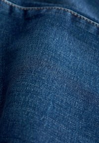 Tissu en denim bleu foncé avec une surface texturée. Présente des coutures contrastantes le long des bords et un léger éclat.
