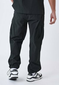 Sorte cargo bukser med en struktureret overflade, der har flere sidelommer og elastiske manchetter. Båret med kontrastfyldte sorte og hvide sneakers.