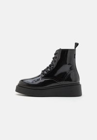Botas de tobillo de charol negro con suela de plataforma negra gruesa, con punta redonda, cordones en la parte delantera y tirador en la parte posterior.