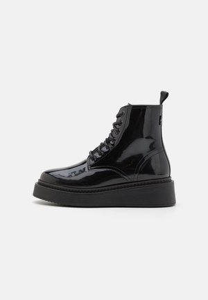 Botas de tobillo de charol negro con suela de plataforma negra gruesa, con punta redonda, cordones en la parte delantera y tirador en la parte posterior.