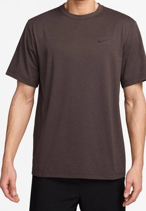 Man draagt een effen donkerbruin T-shirt met korte mouwen en een kleine zwarte Nike-logo op de linkerborst.
