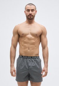 Boxers à carreaux noir et blanc avec une ceinture élastique noire portant le texte "PIER ONE". Le tissu semble doux avec une coupe décontractée.