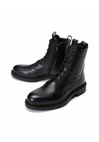 Botas de tobillo de cuero negro con un acabado texturizado, cremallera lateral, cordones en la parte frontal y una suela de goma resistente.