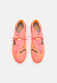 Zapatillas deportivas rosas con un tejido superior texturizado, que presentan detalles en negro, cordones redondos y un forro interior amarillo brillante.