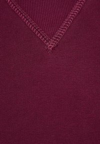 Tessuto a maglia bordeaux con design a V, caratterizzato da una fine trama a coste e cuciture a contrasto lungo il collo.