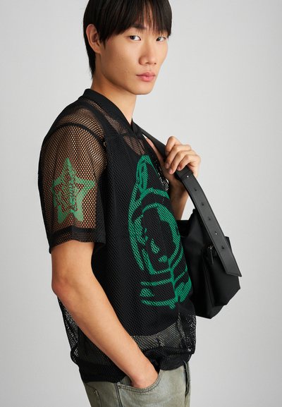 Camisa de malha preta de mangas curtas com designs gráficos verdes. Acompanhada por uma bolsa preta com uma alça, apresentando várias texturas.