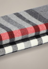 Wełniana tkanina z dwoma wzorami: górna część w szaro-czerwony kratę, dolna w czarno-białą kratę. Miękka faktura z widocznym splotem.