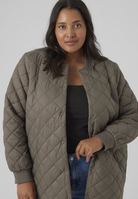 Quilted bomber jacket in muted green with ribbed cuffs and snap buttons. Features a relaxed fit and diamond pattern throughout.