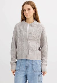 Cárdigan de punto gris claro con un patrón de trenzas, que presenta un cuello alto y cinco botones. Puños y dobladillo acanalados, diseño corto.