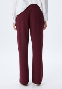 Pantalones de pierna ancha burdeos con cintura elástica, textura suave y corte relajado, mostrados desde la parte posterior con una camisa blanca metida.