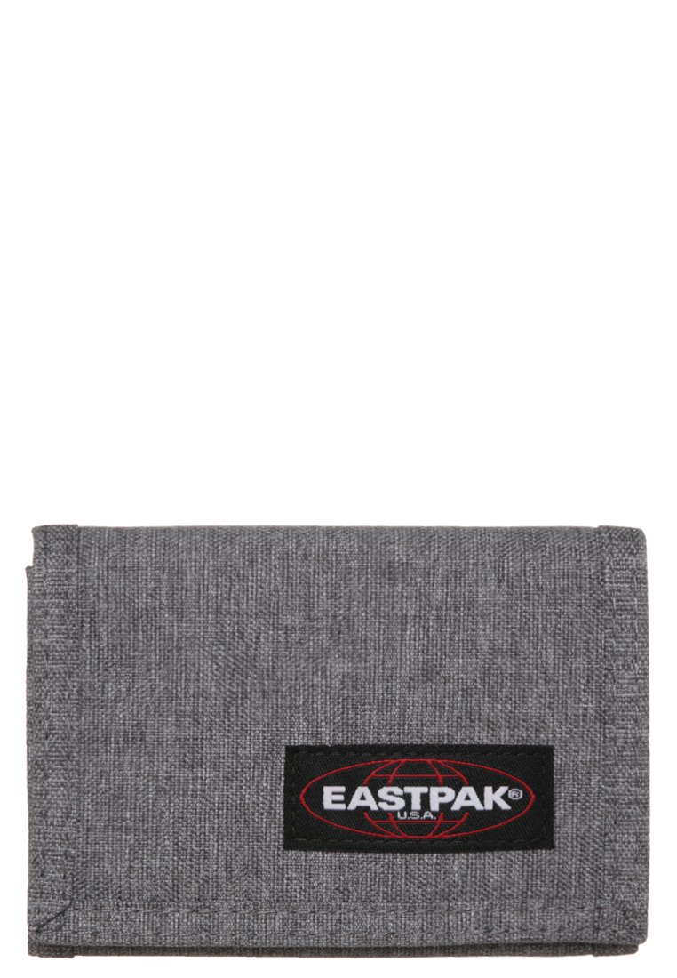 Billetera de tela gris con una superficie texturizada y un parche de logo negro de Eastpak con acentos rojos. Diseño compacto y rectangular con esquinas redondeadas.
