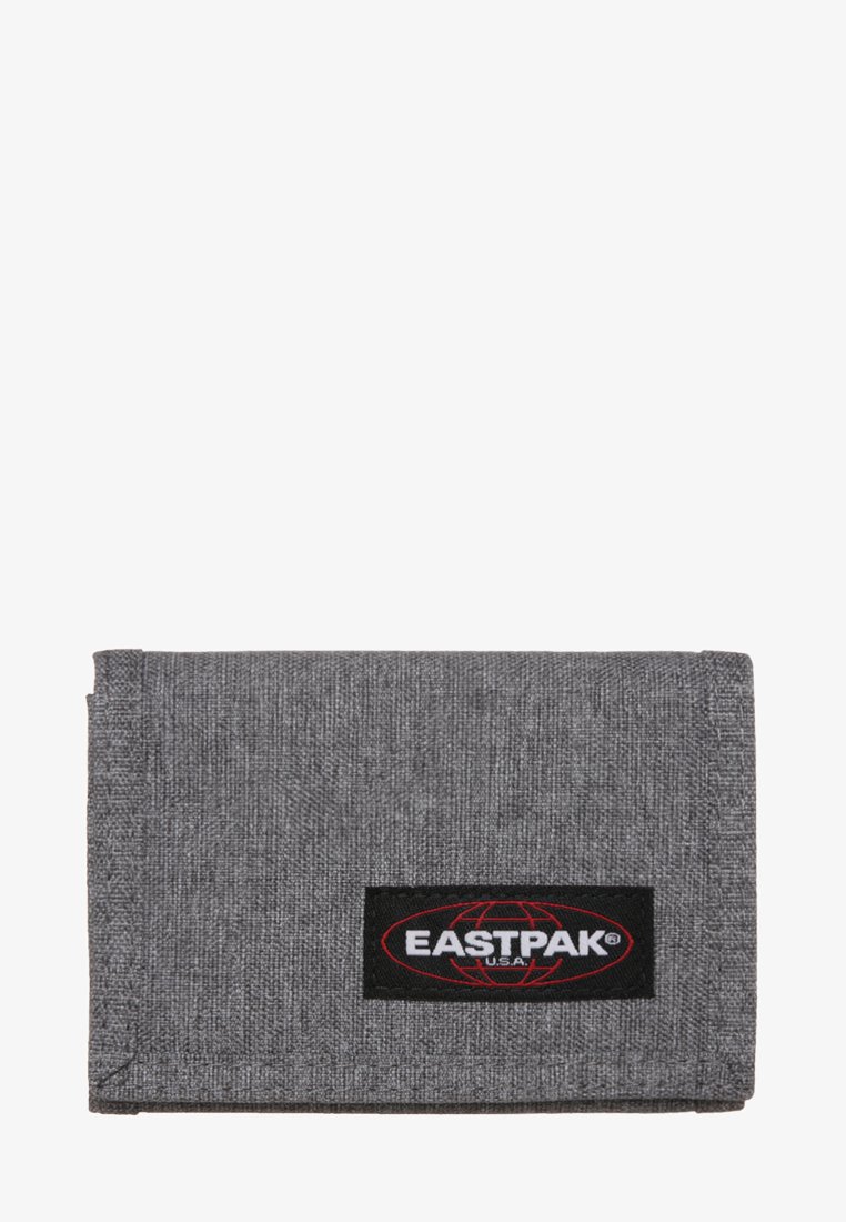 Billetera de tela gris con una superficie texturizada y un parche de logo negro de Eastpak con acentos rojos. Diseño compacto y rectangular con esquinas redondeadas.