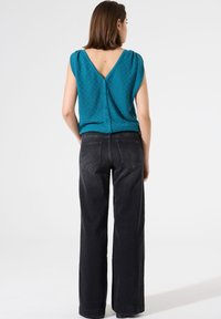 Top corto de color verde azulado, con mangas cortas, textura y escote en V, con cierre de botón en la parte posterior, combinado con jeans negros de tiro alto y pierna recta.