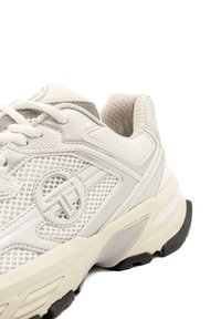 Weißer Sportschuh mit einem Mesh-Obermaterial, strukturierten Akzenten und einer gepolsterten Sohle mit einer schwarzen Gummisohle. Dezentes Markenlogo sichtbar.