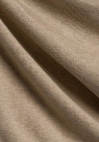 Beige Stoff, der in Falten drapiert ist, mit einer weichen Textur und einem feinen Strickmuster, was auf ein leichtes und atmungsaktives Material hinweist.