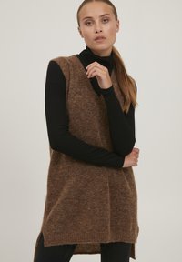Brun uld udenærmede vest med en struktureret overflade og sideslids, lagd ovenpå en sort ribbet turtleneck. Casual pasform og design.