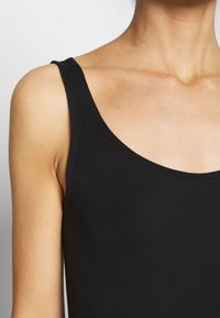 Czarny top bez rękawów z okrągłym dekoltem, wykonany z gładkiej tkaniny. Posiada dopasowany krój i miękką teksturę, idealny do noszenia na co dzień lub do warstwowego ubierania.