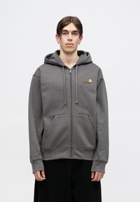 Siva zip-up ljubavni sako napravljen od pamučne mešavine, sa dva prednja džepa, kapuljačom sa vezicom i malim vezom logotipom na grudima.