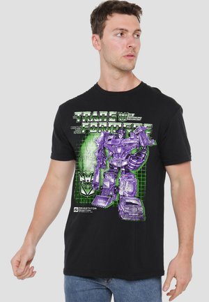 Black t-shirt featuring a graphic of a purple robot transforming, with green grid background and "Transformers" text, made of cotton material.