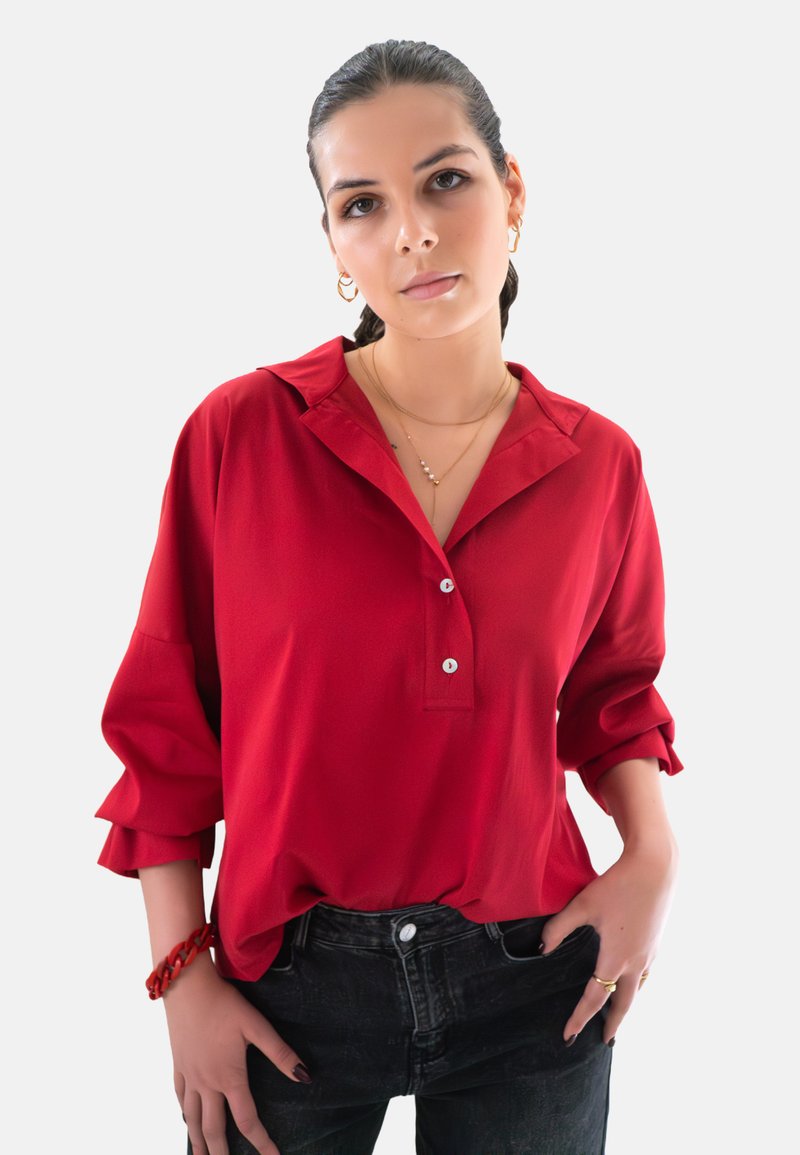 Rode blouse met een kraag, knoopsluiting en opgerolde mouwen. Gemaakt van soepele stof, met een relaxte pasvorm. Draagt met donkere jeans.