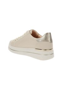 Baskets beiges avec accent métallique au talon, bout rond et lacets. Elles présentent une semelle blanche avec une bande d'accent dorée. Texture lisse.
