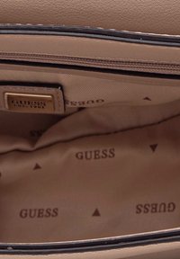 Interno di una borsa beige con una texture morbida. Presenta un motivo a logo marrone e un scomparto con zip. Inclusi accenti triangolari sottili.
