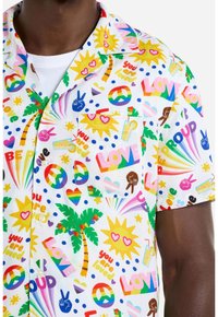 Camicia a maniche corte con colletto, caratterizzata da un vivace motivo multicolore con palme, cuori, arcobaleni e frasi motivazionali su uno sfondo bianco.