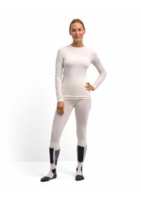 Top bianco a maniche lunghe e leggings in tessuto texturizzato, accompagnati da calzini multicolore con accenti grigi e neri.