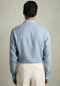 Lichtblauwe katoenen shirt met verticale witte strepen, met knoopmanchetten en een klassieke kraag, gecombineerd met crèmekleurige broeken.