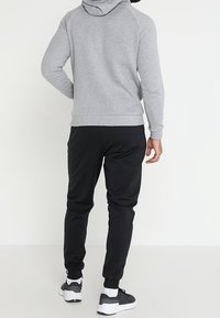 Sudadera gris con capucha y mangas raglán, combinada con joggers deportivos negros. Ambos están hechos de una tela suave, con puños y cinturilla elásticos.