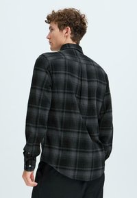 Black and gray plaid flannel shirt featuring a button-down collar, long sleeves, and a curved hem. Soft texture with a classic check pattern.
