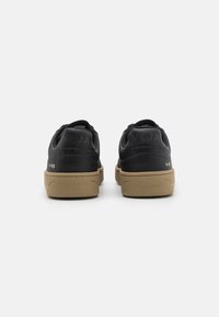 Sorte lær sneakers med teksturert overflate, med en tan gummisåle og preget logo detalj på hælen. Enkelt, klassisk design.