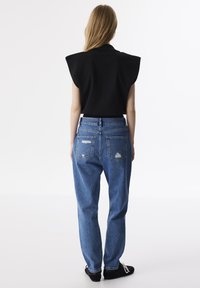 Top negro con hombreras combinado con jeans de tiro alto en azul desgastado que presentan bolsillos traseros y detalles deshilachados. Zapatos negros.
